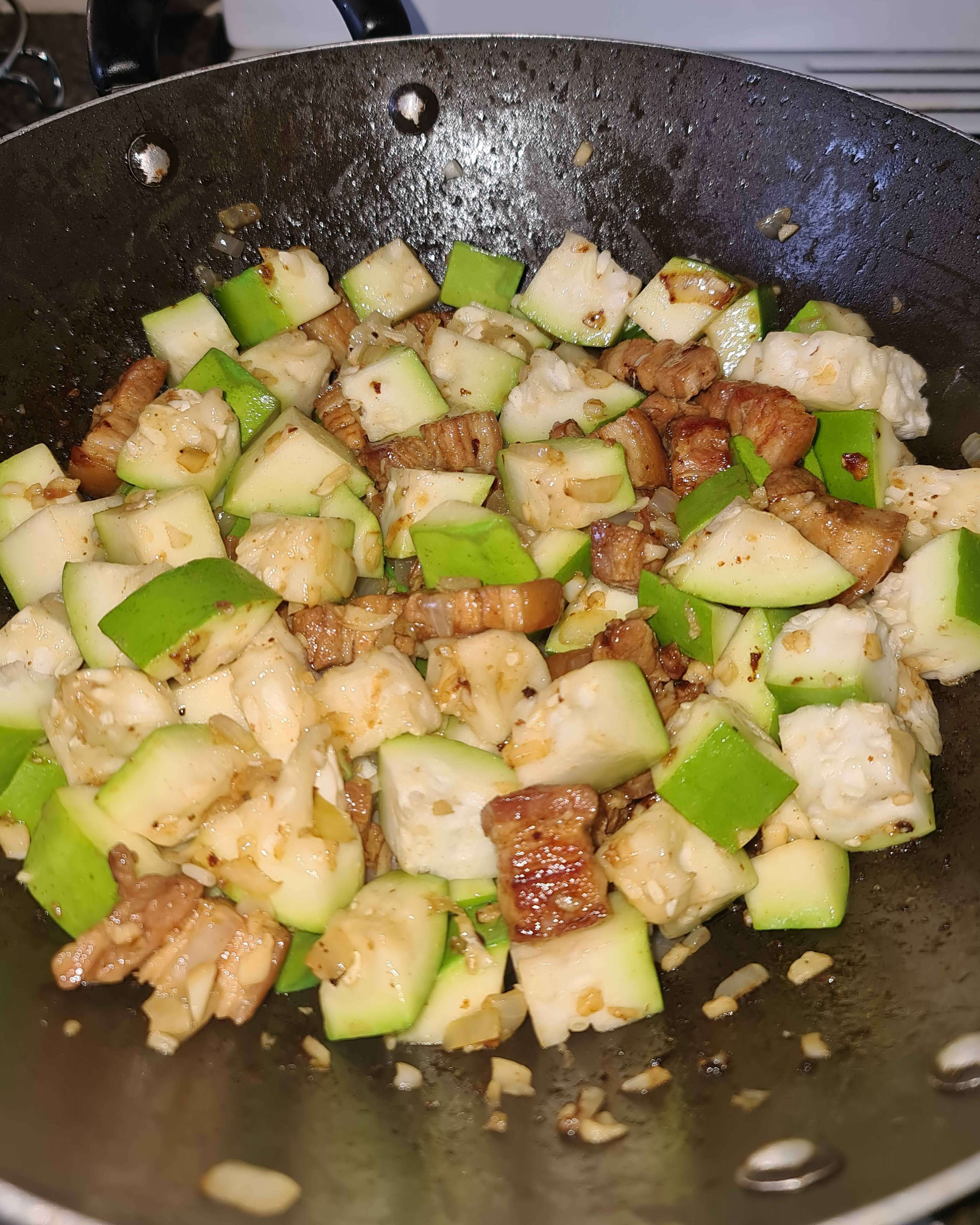 A picture of cooked pork in a wok, where upo has just been added and stirred.